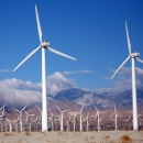 Wind farm in sand dunes with mountain range in background.