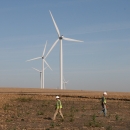 People searching a plot around a wind turbine with wind turbines in the background.