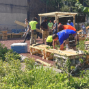 people in colored shirts work in a gravel lot building wooden structures