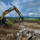 Heavy equipment on a dirt landscape with green vegetation and blue skies above