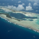 Aerial view of an island atoll surrounded by sandy reef in the deep blue ocean