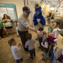 A smiling uniformed refuge ranger hands junior ranger badges out to a group of children.