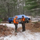 Two men wearing blaze orange in front of a hunting camp.