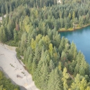 An aerial view of a dry creek on the left and a blue body of water on the right, separated by green trees.