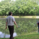 Service employee in refuge browns watches as young boy casts fishing pole into pond.