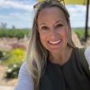 A woman in a green dress with blonde hair smiles at the camera