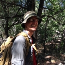 A man with a hat and backpack on in a forest smiling