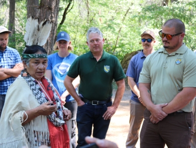 Several people stand in a circle around a woman wearing traditional Tribal garments