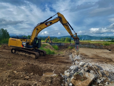 Heavy equipment on a dirt landscape with green vegetation and blue skies above