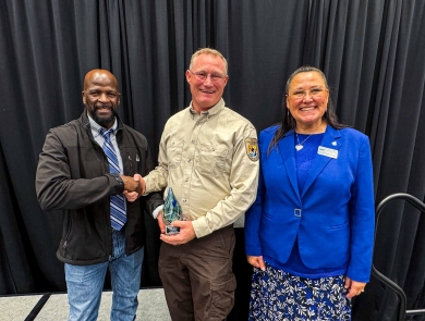 A unformed FWS employee shakes hands with another individual while holding an award. A woman stands smiling to the right of the awardee.