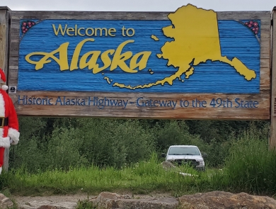 Watercraft inspector, Steve Wogtech, posed in Santa suit in front of Welcome to Alaska sign.