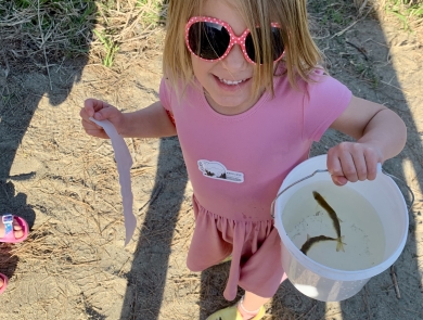 Young girl in a pink dress holds a small bucket with two fish to release