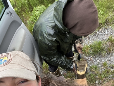 Biologist smiling while lifting a boot up to have friend clean dirt out of tread. 
