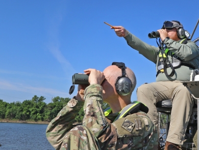 2 men sitting in boat using binoculars, using headphones