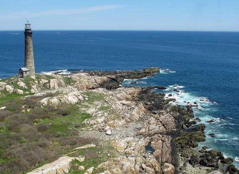 A lighthouse on a cliff overlooking the deep blue ocean under a clear sky