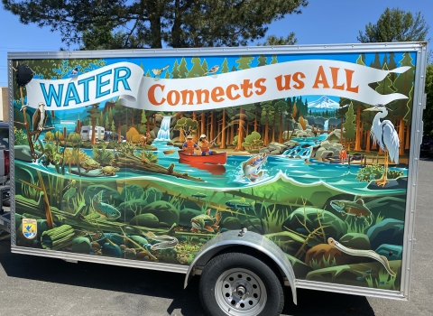 Trailer with wrap-around artwork depicting a river full of wildlife above and below the waterline, with people recreating and text that reads "Water Connects Us All"