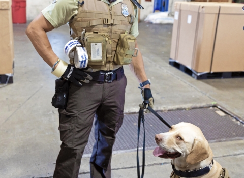 Officer standing with this dog on a leash in a warehouse.