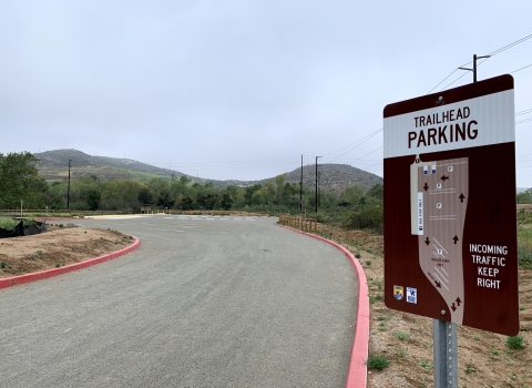 Trailhead parking sign with map on the side of the road entering the refuge parking lot.