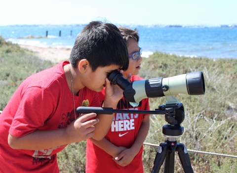 Two young boys use a spotting scope 