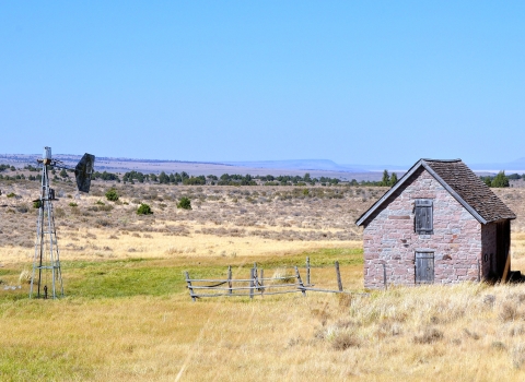 An old stone A-framed building in a high desert landscape with an old mill next to it