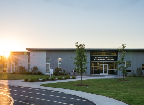 he left side of a brick-and-mortar buidling is illuminated by the sunrise peeping above the treeline.