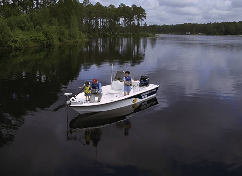 Family fishing in a boat on a body of water with woody landscape in the background. 