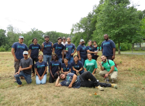 a group of people wearing purple and green shirts standing in a green field of a nature park