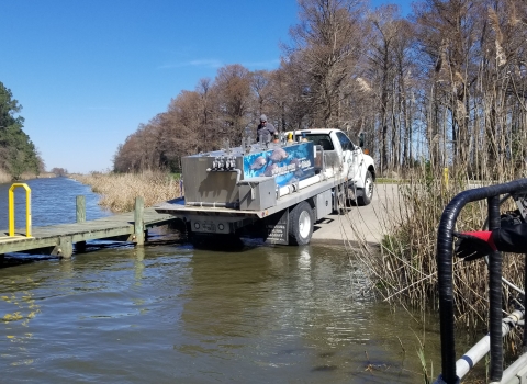 A truck with a large metal tank banks into a boat launch.