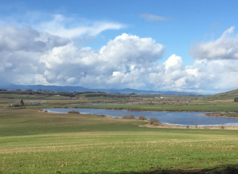 Wide view of prairie with pond in the distance on a partly cloudy day.
