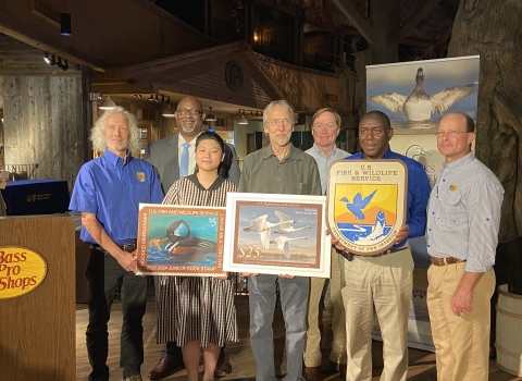 Group photo of people holding duck stamp arts and USFWS logo.