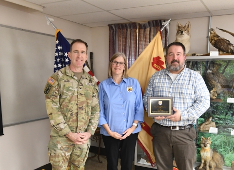 Three people stand together, one holding an award plaque
