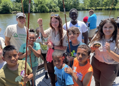 Youth pose with a fish and U.S. Fish and Wildlife Service staff at the 2024 Cops and Bobbers Fishing Program
