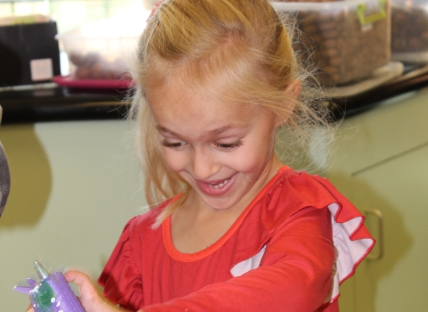 A blond haired girl is using a hot glue gun to make an ornament