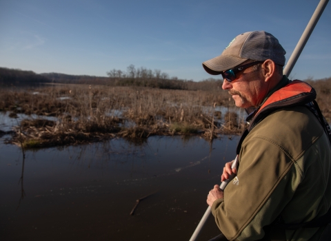 Biologist stands on the front of a boat with net to catch fish. 