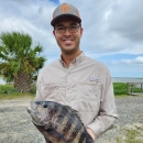Man wearing a hat and glass holding a large fish with vertical black and gray bar stripes