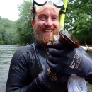 Person wearing wetsuit, gloves, and swimming mask and snorkel and holding a large Eastern hellbender in hands.