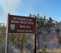 Photo of drone flying over active fire next to Marsh Trail sign.