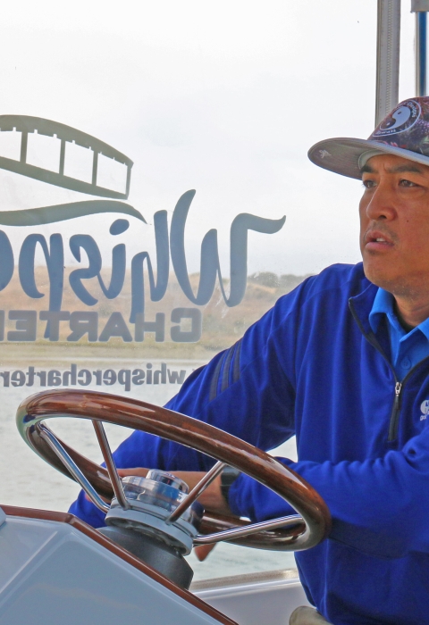 A man wearing a blue jacket driving a boat