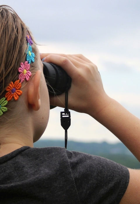 A young woman looking through binoculars along a railing