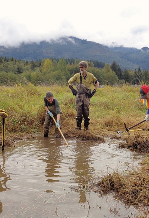 A group of people standing around standing water in a wetland area