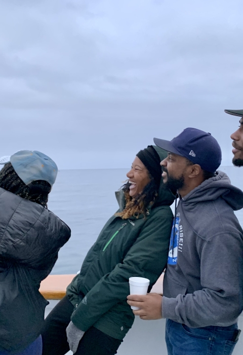 Four members of the organization stand next to each other and take a selfie. The ocean view is in the background.