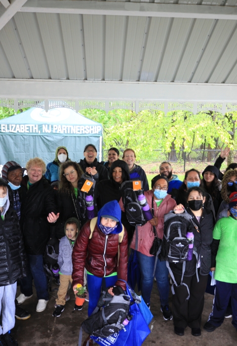 A large group of people standing under a pavilion smiling. A tent is seen in the background with the words "Elizabeth NJ Partnership" printed on the front