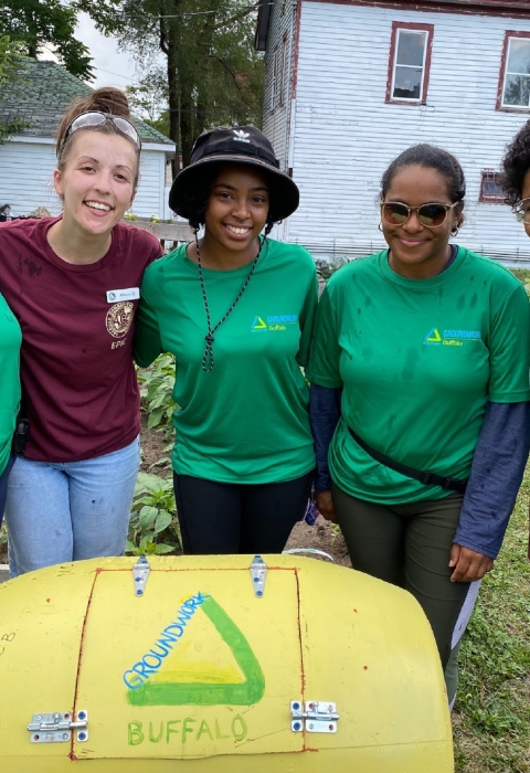 5 people stand with arms around each in front of a yellow barrel-shaped object with the words "groundwork Buffalo" written on it