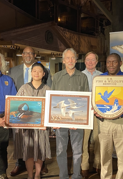 Group photo of people holding duck stamp arts and USFWS logo.