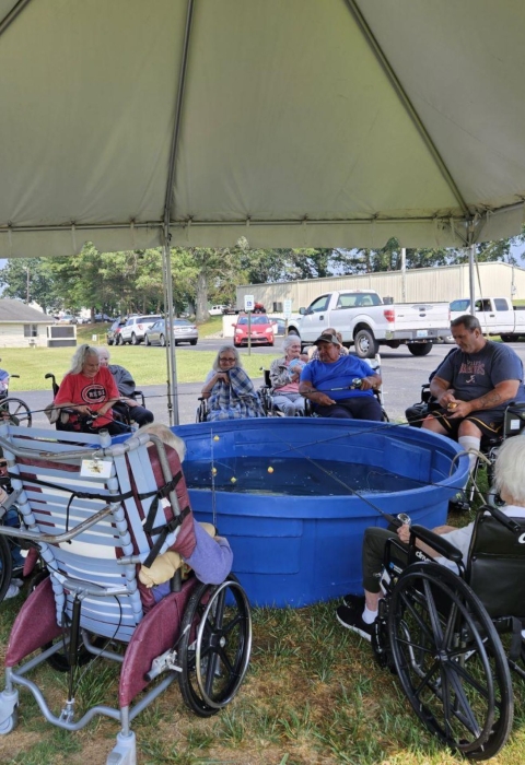 Elderly people fishing out of blue stock tub under a tent