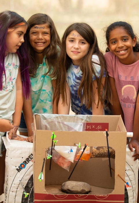 Four Nature Niños students stand for a photo with the arrows they shot during archery practice. 