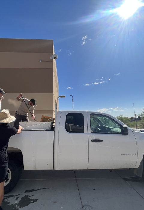 Two Service employees standing in the back of a truck preparing to unload fish from the truck's tank.