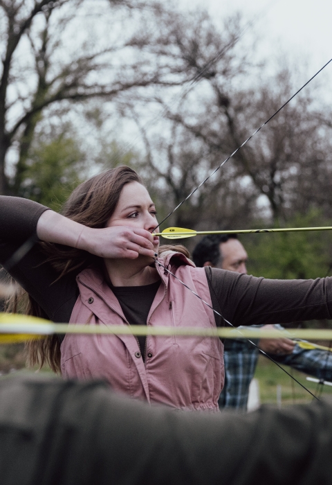 Female archer lines up with other archers and takes aim at target.