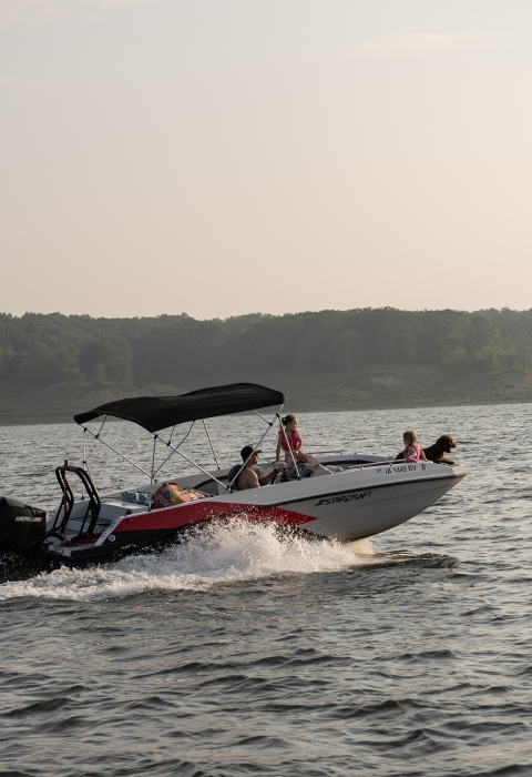 Family with children and a dog riding on a speedboat across a lake. 