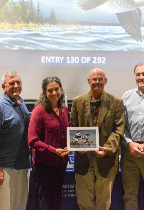 Six judges at the 2025 Federal Duck Stamp Art Contest hold the winning artwork.